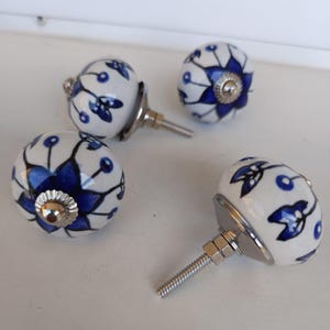 May include: Four round ceramic cabinet knobs featuring a white base with a hand-painted blue floral pattern. Each knob has a metallic silver-toned base and a threaded metal bolt extending from the back for installation on furniture or doors.