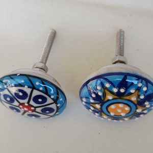 Peut inclure: Deux boutons de placard ronds en c&eacute;ramique avec des motifs peints &agrave; la main. Le bouton de gauche pr&eacute;sente un motif g&eacute;om&eacute;trique bleu, blanc et rouge. Le bouton de droite affiche un motif en &eacute;toile bleu, jaune et blanc. Inclut boulon et &eacute;crou.
