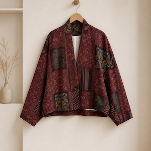May include: A burgundy patchwork jacket featuring a variety of dark-toned patterns including floral, geometric, and striped motifs. The jacket has a wide collar, long sleeves, a single front button closure, and a white interior lining.