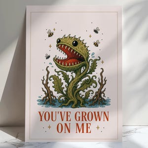 Può includere: Una stampa artistica rettangolare raffigurante una pianta carnivora verde con la bocca spalancata, denti affilati e grandi occhi. La pianta è circondata da piccole api e acqua. Il testo "YOU'VE GROWN ON ME" è stampato in rosso in basso.