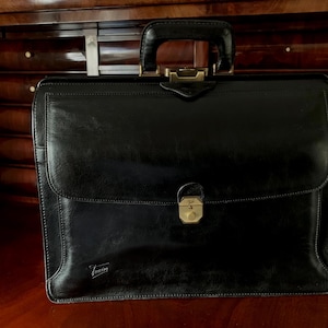 Pasta/Porta-documentos Texier em couro preto com fecho de pressão, alça superior e bolsos internos.
