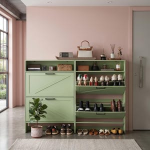 May include: Two sage green shoe storage cabinets with drop-down doors and black handles. The left unit is closed, while the right unit is open, displaying multiple pairs of shoes on shelves. A potted plant sits on the floor next to the cabinets.