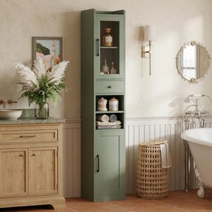 May include: A tall, sage green bathroom storage cabinet featuring a top glass-paneled door, a single central drawer, two open shelves, and a bottom solid door. The unit includes black hardware and is designed for vertical organization in a bathroom.