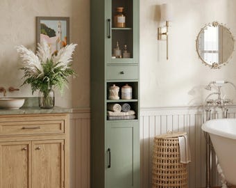 Puede incluir: Un armario de baño alto en color verde salvia con una puerta superior de cristal, un cajón central, dos estantes abiertos y una puerta inferior sólida. La unidad incluye herrajes negros y está diseñada para el almacenamiento vertical.