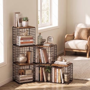 May include: A modular storage unit composed of five stacked black metal wire cubes with dark wood shelves. The unit holds various books, including titles like Impressionism and Modern Art, a small potted succulent, a ceramic bird, and vases.
