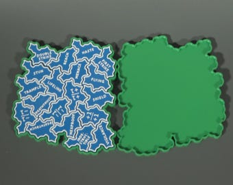 Könnte beinhalten: Zwei unregelmäßig geformte, wolkenartige Spielmarker. Ein Marker ist einfarbig grün. Der andere ist blau mit weißen Umrandungen und Text, der die Spielbegriffe Double Strike, Haste, First Strike, Flying, Shield, Vigilance, Indestructible, Hexproof, Menace, Reach, Stun, Trample, Lifelink, Deathtouch sowie die Symbole +1/+1 und -1/-1 enthält.