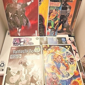 May include: A collection of comic books including Absolute Superman, Batman, and Fantastic Four issues. The covers feature various characters in colorful illustrations, with DC and Marvel logos visible on the top corners of the individual comic books.