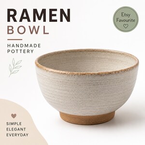 May include: A handmade ceramic ramen bowl with a speckled off-white glaze and a textured, unglazed brown clay base. The bowl features a wide, rounded shape with a slightly flared rim. Text on the image reads RAMEN BOWL HANDMADE POTTERY.