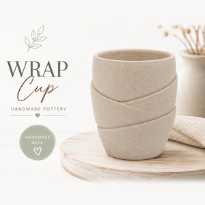 Könnte beinhalten: Ein beigefarbener Keramikbecher mit strukturierter, gesprenkelter Oberfläche und einem geschichteten Wickeldesign. Der Text WRAP Cup HANDMADE POTTERY sowie ein kreisförmiges Abzeichen mit dem Text HANDMADE WITH sind links zu sehen.