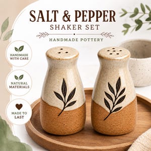 Könnte beinhalten: Ein Salz- und Pfefferstreuer-Set aus handgefertigter Keramik mit zweifarbiger beiger und brauner Oberfläche. Jeder Streuer zeigt ein dunkelbraunes Blattmotiv und den Text SALT & PEPPER SHAKER SET HANDMADE POTTERY, HANDMADE WITH CARE, NATURAL MATERIALS, MADE TO LAST.