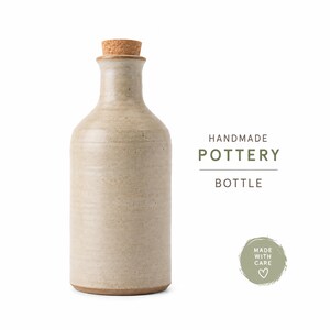 May include: A beige ceramic bottle with a cork stopper. The text HANDMADE POTTERY BOTTLE is printed to the right, along with a circular green emblem containing the text MADE WITH CARE and a small heart icon, all on a plain white background.