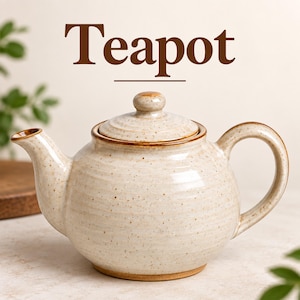 May include: A round ceramic teapot with a speckled cream finish and brown rim accents. The teapot features a matching lid with a small knob, a curved handle, and a spout. The word Teapot is printed in large brown letters above the object.