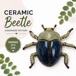May include: A ceramic beetle figurine featuring a glossy, dark blue abdomen and a light green, mottled thorax. The insect has six articulated legs and two small antennae, all finished with a smooth, reflective glaze and dark brown accents.