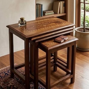 Peut inclure: Un ensemble de deux tables gigognes rectangulaires en bois brun foncé. Chaque table présente une surface lisse avec des motifs floraux incrustés de couleur claire le long des bords. Les tables ont quatre pieds droits et un cadre robuste.