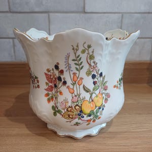 May include: A white ceramic planter with a scalloped rim and base, featuring a colourful botanical illustration of various fruits, berries, and flowers including apples, blackberries, and rose hips, finished with a delicate gold trim.