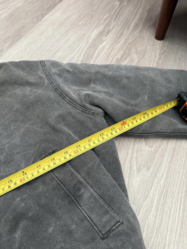 May include: A charcoal gray jacket with a visible seam and a pocket, measured by a yellow tape measure showing a length of approximately 28 inches from the shoulder area to the sleeve cuff, indicating the garment's scale in a clear, objective view.
