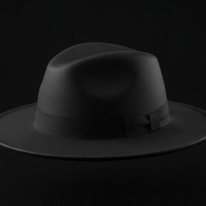 May include: A solid black fedora hat featuring a structured crown with a central crease and a wide, flat brim. A matching black grosgrain ribbon band encircles the base of the crown, providing a uniform and monochromatic appearance throughout the design.