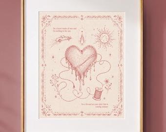 May include: A framed art print featuring a red ink illustration on a cream background. The central image is a dripping heart connected by thread to a spool, surrounded by a sun, a flame, and text. The frame is gold with a white mat border.