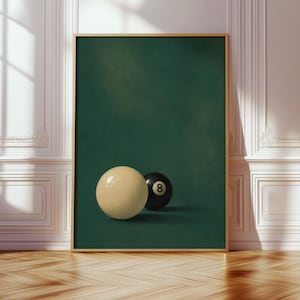 May include: A framed vertical wall art print featuring a solid cream-colored cue ball positioned in front of a black eight ball with a white number eight. The background is a deep, solid forest green, and the frame is a thin, metallic gold color.