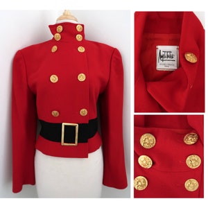 Könnte beinhalten: Ein roter zweireihiger Blazer mit goldenen Knöpfen und einem schwarzen Gürtel. Das Etikett lautet "Angel Estrada Paris".