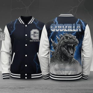 Op de afbeelding: Een marineblauw en wit varsity-jack met een afbeelding van Godzilla op de achterkant en de tekst Godzilla King of the Monsters. De voorkant toont een letter G met de tekst King of the Monsters en witte mouwen met gestreepte boorden.