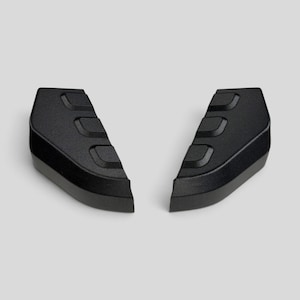 May include: Two black, textured plastic components with a curved, angular shape. Each piece features three distinct, raised rectangular indentations along the top surface, designed with a matte finish and a solid, durable construction.