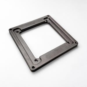 May include: A dark grey square frame with a textured surface and a hollow centre. The frame features four circular holes at the corners and a recessed inner border with additional small circular openings, showing a layered construction.