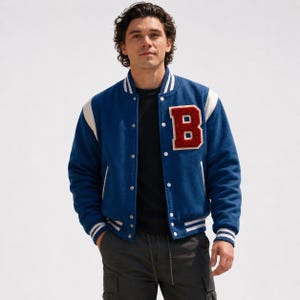 May include: A blue varsity jacket featuring white sleeves, a red letter B patch on the chest, and white striped ribbed trim on the collar, cuffs, and hem. The jacket has a snap-button front closure and is worn over a black shirt and dark pants.