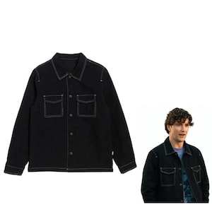 Op de afbeelding: Een zwart jack met lange mouwen, voorzien van een klassieke kraag, een knoopsluiting aan de voorzijde en twee borstzakken met kleppen. Het kledingstuk is afgewerkt met opvallende witte contraststiksels langs de naden, zakken en manchetten.