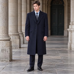 May include: A dark navy blue wool overcoat worn over a matching suit jacket, vest, and trousers. The ensemble includes a light blue button-down shirt and a dark grey striped necktie, paired with polished black leather dress shoes.