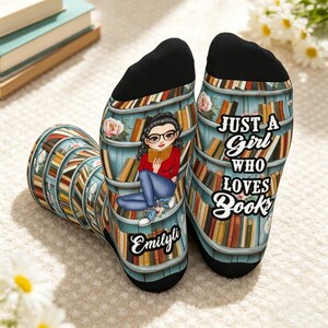 May include: A pair of black-heeled socks featuring a bookshelf print with a cartoon character reading a book, the name "Emilyli," and the text "JUST A GIRL WHO LOVES BOOKS" in white lettering. The socks have a black toe and heel section.