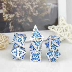 May include: A set of seven polyhedral dice featuring a metallic silver finish with bright blue enamel inlays. Each die displays intricate raised patterns and clear numerical markings. The collection includes various shapes such as a d20, d12, d10, d8, d6, and d4, arranged in three small stacks on a white surface.