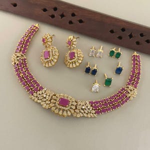 Peut inclure: Un collier doré composé de trois rangées de pierres rectangulaires magenta et d'ornements floraux avec des cristaux clairs. L'ensemble comprend deux boucles d'oreilles assorties et six paires de clous d'oreilles avec des pierres magenta, vertes, bleues et claires.
