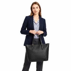 Puede incluir: Un bolso tote negro con silueta estructurada, que cuenta con dos asas superiores sujetas mediante hebillas metálicas. El bolso tiene un acabado liso, una abertura amplia y esquinas reforzadas en la base, ofreciendo un diseño limpio y funcional.