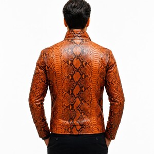 May include: A long-sleeved jacket featuring a vibrant orange and black snakeskin pattern. The garment has a high collar, a structured fit, and a full-length zipper closure, shown from the back view against a plain white background.