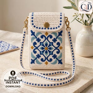 Può includere: Una borsa a tracolla all'uncinetto color crema con un motivo floreale a piastrelle blu, azzurro e giallo. La borsa presenta una patta con chiusura a scatto dorata, una tracolla abbinata con dettagli blu e ganci girevoli in metallo dorato.