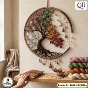 Puede incluir: Un tapiz circular con un &aacute;rbol tejido a ganchillo que representa las cuatro estaciones con flores rosas, hojas verdes, follaje oto&ntilde;al naranja y rojo, y ramas invernales blancas, decorado con colgantes de estrellas, luna y borlas.