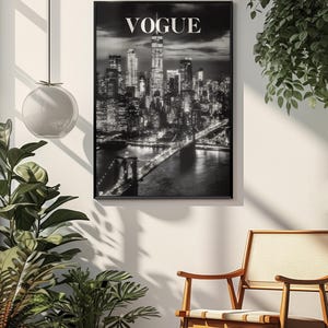 May include: A black and white framed wall art print featuring a nighttime cityscape of New York City with the Brooklyn Bridge in the foreground and the word VOGUE printed in white capital letters at the top center of the rectangular composition.