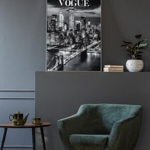 May include: A framed black and white wall art print featuring a nighttime cityscape of New York City with the Brooklyn Bridge in the foreground and the word VOGUE printed in white capital letters at the top center of the rectangular image.