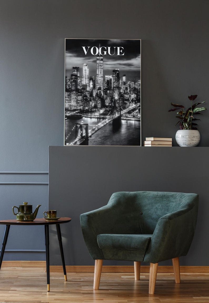 May include: A framed black and white wall art print featuring a nighttime cityscape of New York City with the Brooklyn Bridge in the foreground and the word VOGUE printed in white capital letters at the top center of the rectangular image.