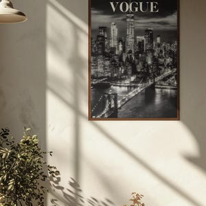 May include: A rectangular wall art print featuring a black and white night cityscape of New York City, including the Brooklyn Bridge and the Manhattan skyline, with the word VOGUE printed in white capital letters at the top center of the image.