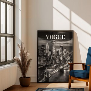 May include: A framed black and white wall art print featuring a nighttime cityscape of New York City with the Brooklyn Bridge in the foreground and the word VOGUE printed in white capital letters at the top center of the composition.