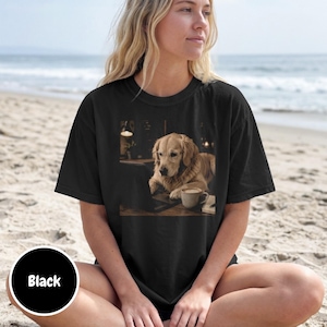 May include: A black short-sleeve t-shirt featuring a graphic print of a golden retriever dog sitting at a desk with a laptop and a coffee mug. The shirt has a crew neckline and a relaxed fit, showcasing a detailed illustration of the dog.