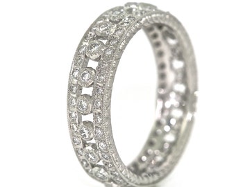 Könnte beinhalten: Ein silberner Bandring mit einem zarten Design, das eine Reihe von runden Diamanten zeigt, die in einem durchgehenden Muster gesetzt sind. Der Ring ist mit filigranen Details gearbeitet und strahlt zeitlose Eleganz aus.