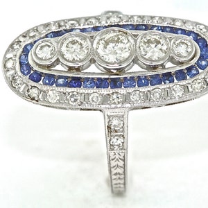 May include: A silver ring with a large oval-shaped setting featuring five round diamonds and a border of blue sapphires.
