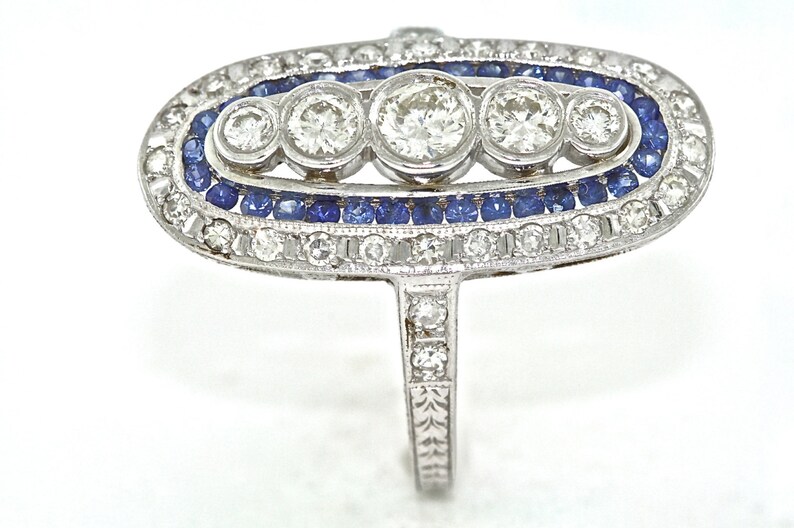 May include: A silver ring with a large oval-shaped setting featuring five round diamonds and a border of blue sapphires.