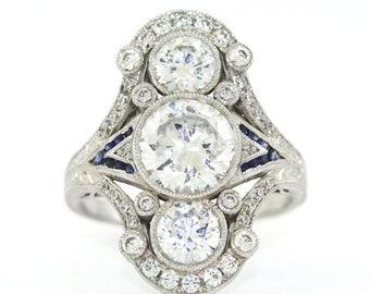 May include: A silver ring with three round diamonds and blue sapphires set in a delicate, ornate design.
