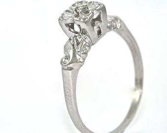 Pode incluir: Um anel de prata com um design delicado e ornamentado. O anel apresenta um único diamante redondo engastado em garras.