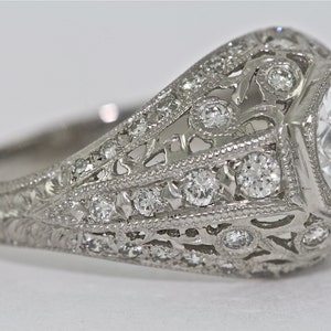 May include: A silver ring with a large, clear, octagon-shaped center stone surrounded by smaller diamonds. The band is intricately designed with filigree details and smaller diamonds.