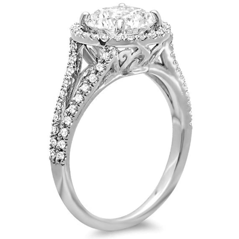 May include: A silver engagement ring with a large round center stone surrounded by a halo of smaller stones. The band is set with smaller stones and has a delicate, intricate design.